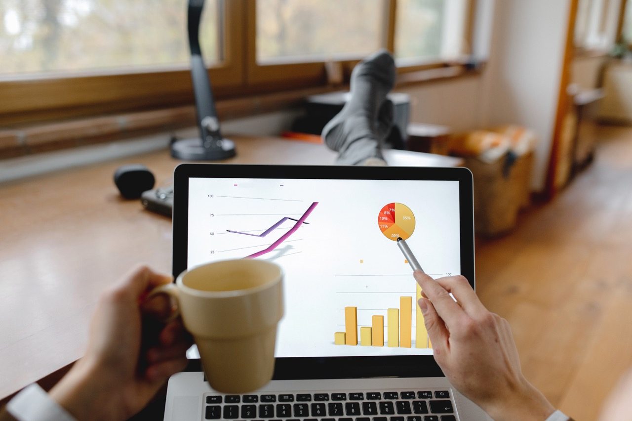 Pessoa acompanhando um gráfico de crescimento no notebook ao lado de uma xícara de café